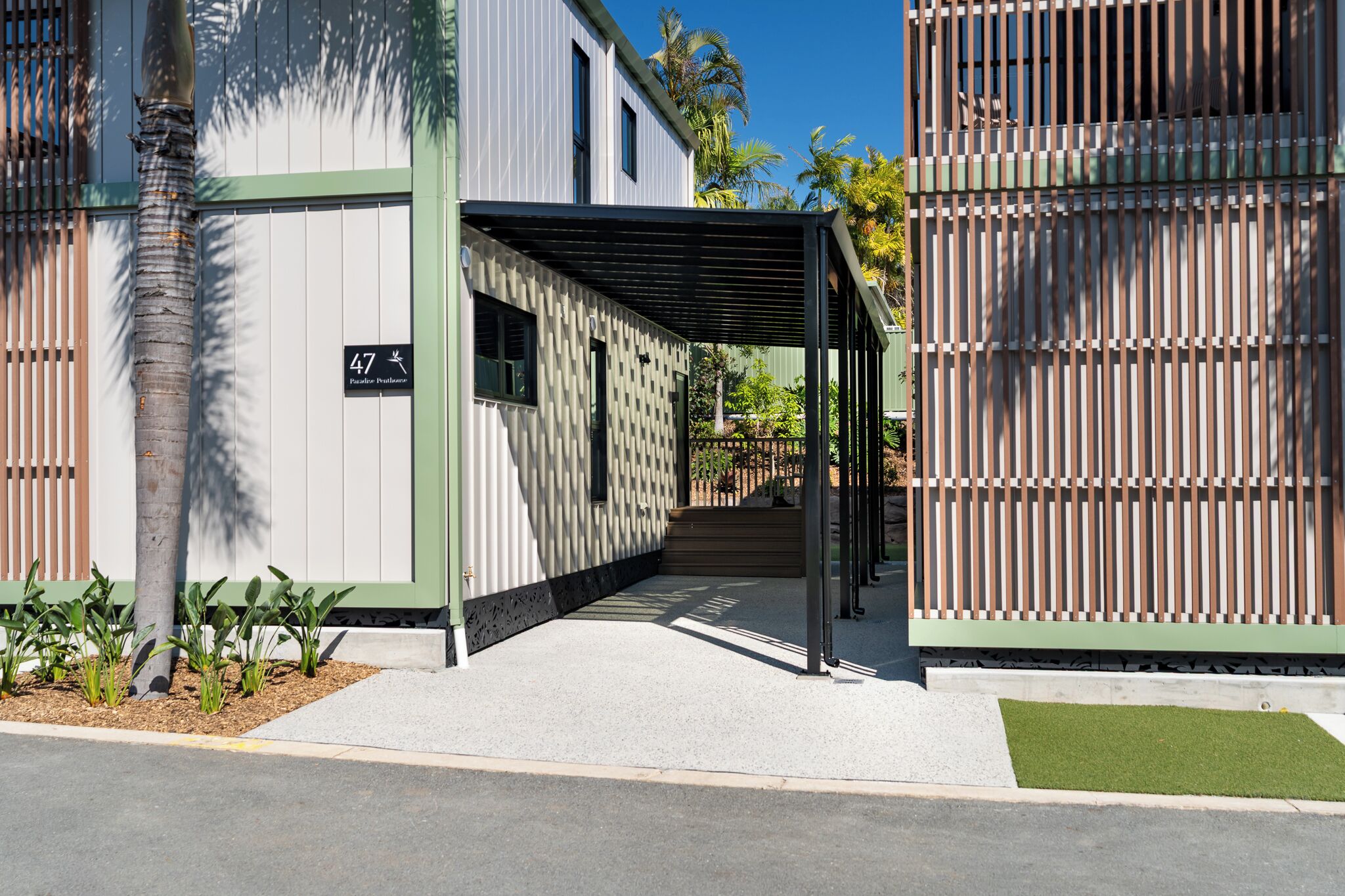 A modern building with a covered entrance, a sign indicating the address, and a pathway leading to the entrance.