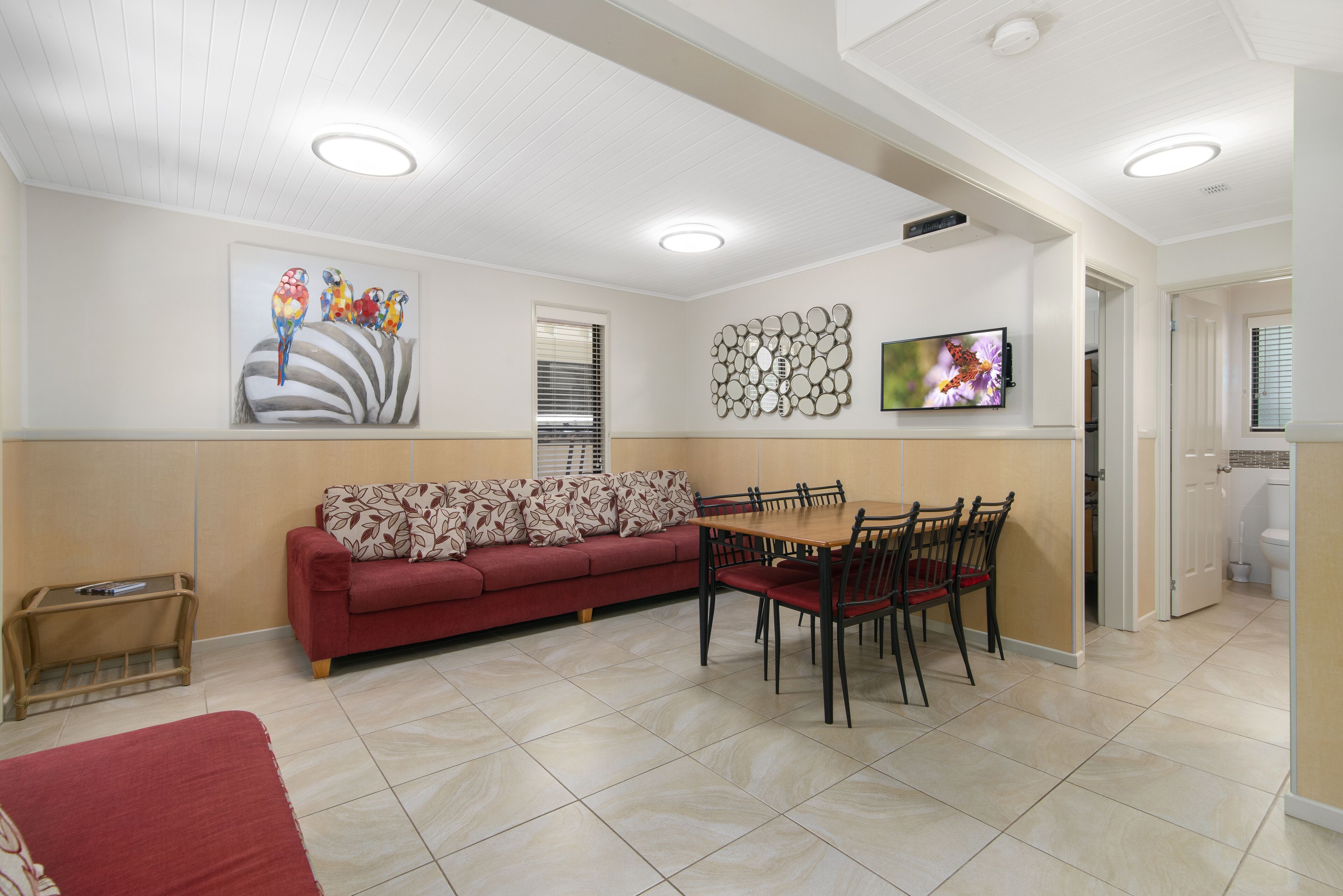 Un área de comedor con un sofá rojo, una mesa de madera con sillas y un televisor en la pared.