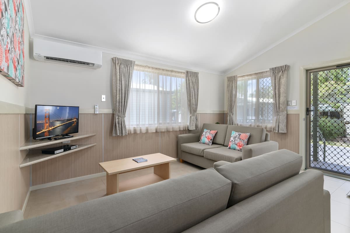 A modern living room with a flat-screen TV, a sofa, a coffee table, and a large window with curtains.