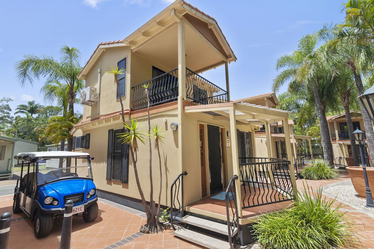 A two-story building with a balcony, a golf cart, and palm trees.