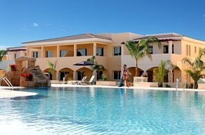 A resort with a swimming pool, palm trees, and a building with multiple balconies.