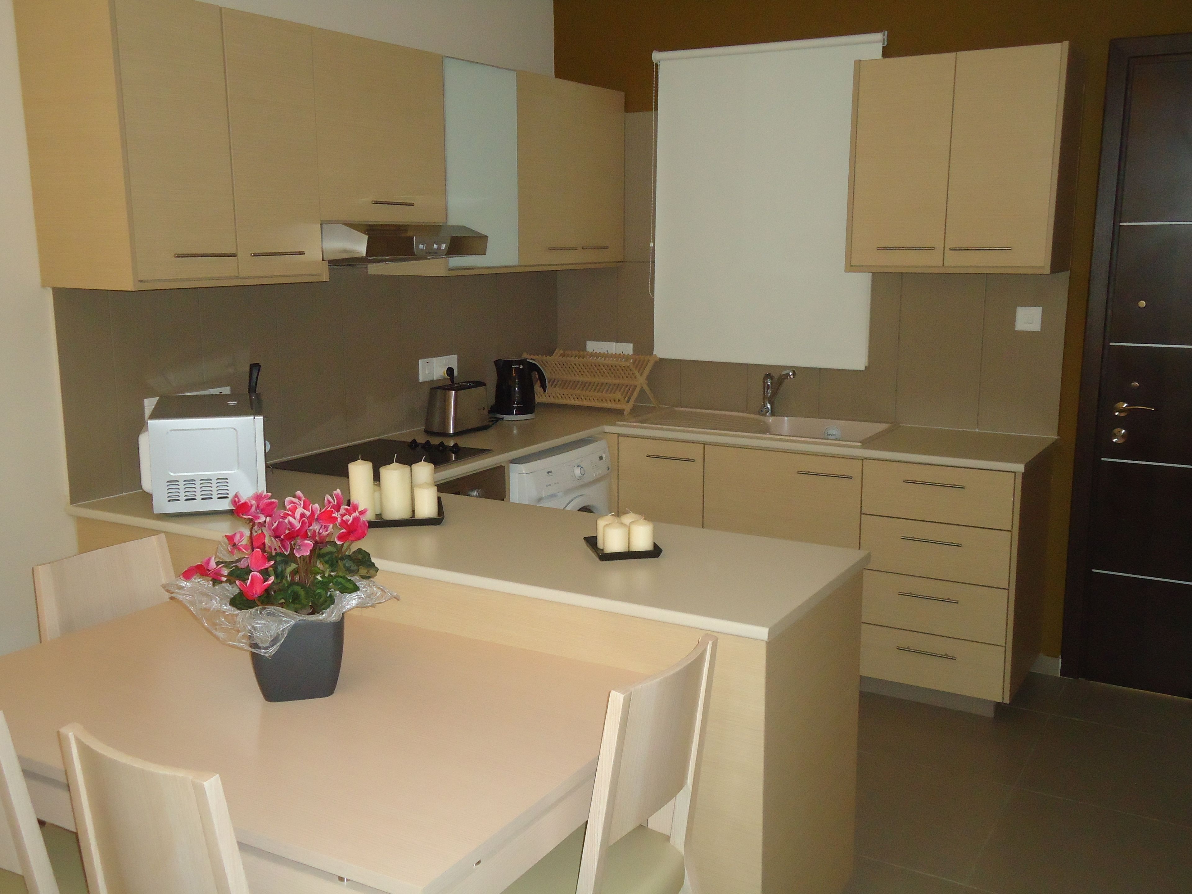 Une cuisine moderne dotée d’un îlot central, d’un évier, d’une cuisinière et d’un four à micro-ondes. On y trouve une petite table avec des chaises et une plante en pot.