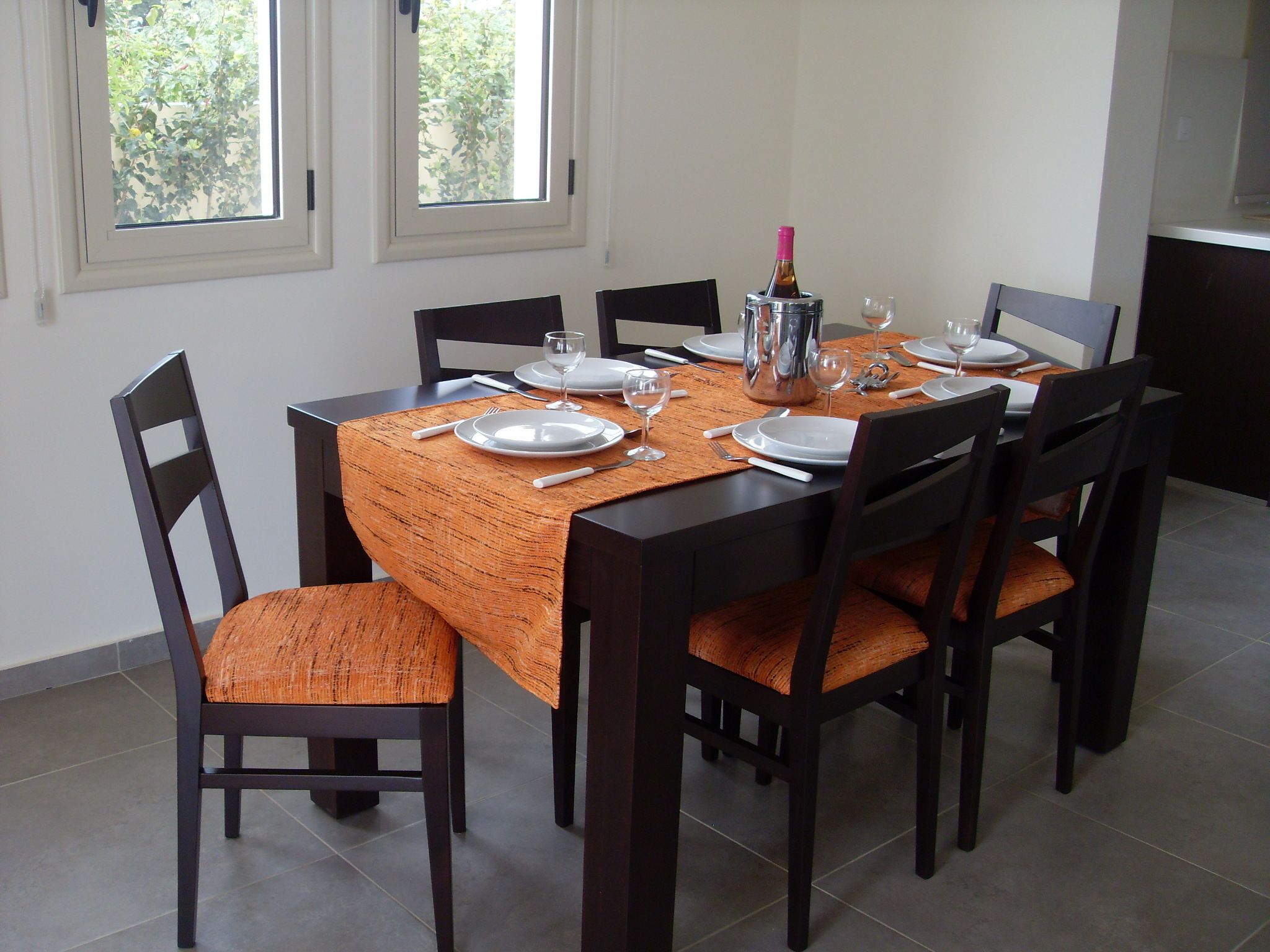 A dining table set for six with chairs, a placemat, plates, cutlery, and a bottle.