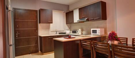 A modern kitchen with dark wooden cabinets, a white countertop, a microwave, and a dining area with wooden chairs and a table.