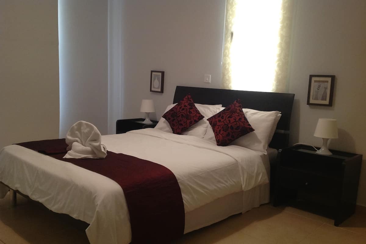 A neatly made bed with white and red bedding, two bedside tables with lamps, and framed pictures on the walls.