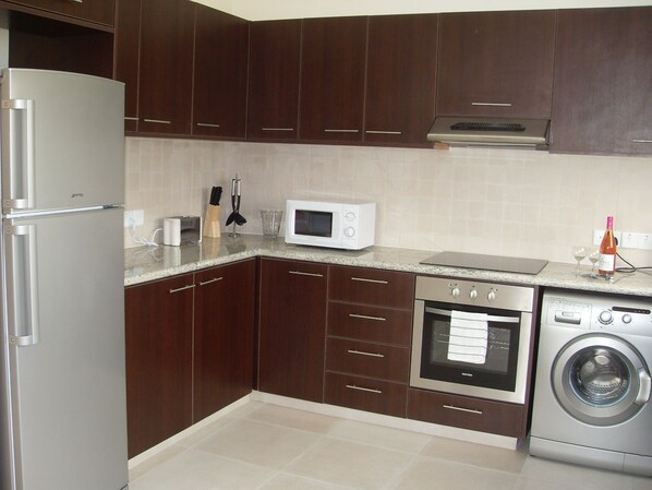 Una cocina moderna con armarios de madera oscura, un refrigerador de acero inoxidable, un microondas, un horno y una lavadora.