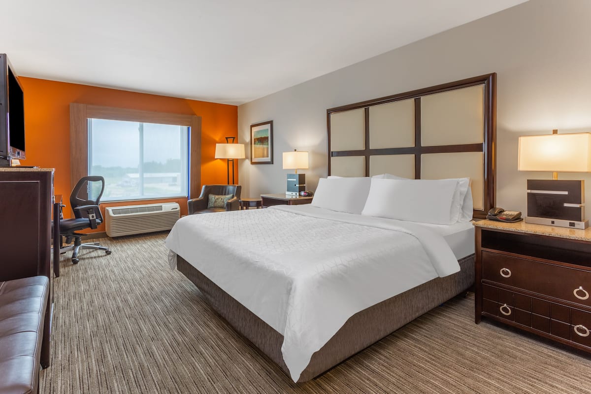 Een hotelkamer met een groot bed, een bureau, een stoel, een bureaulamp, een nachtkastje en een raam met uitzicht.
