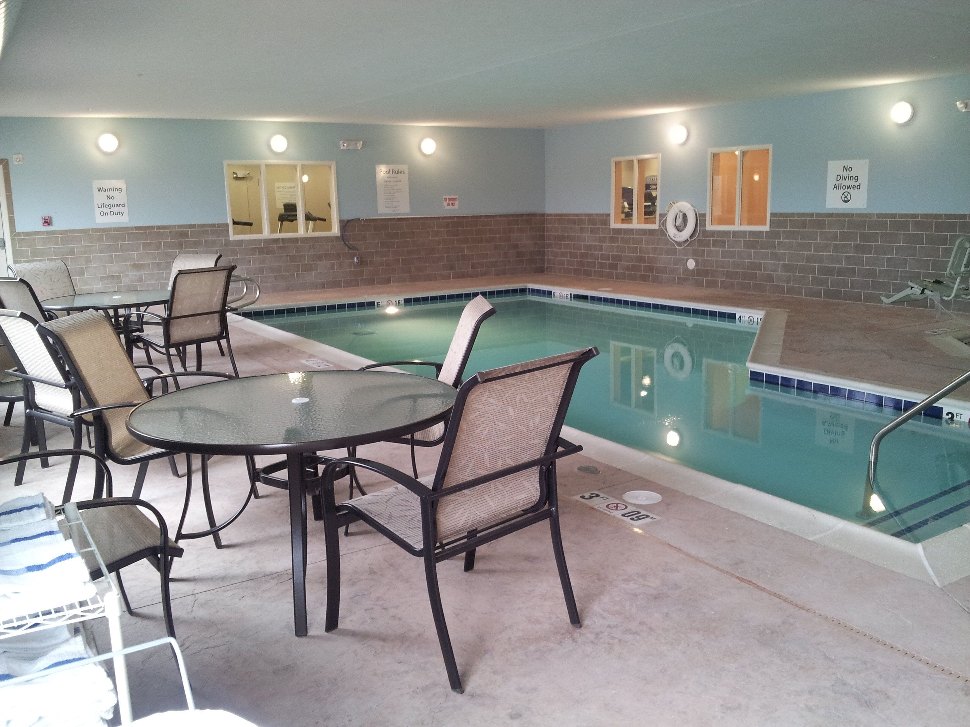 An indoor pool area with chairs and tables, a lifeguard on duty sign, and pool rules posted on the wall.
