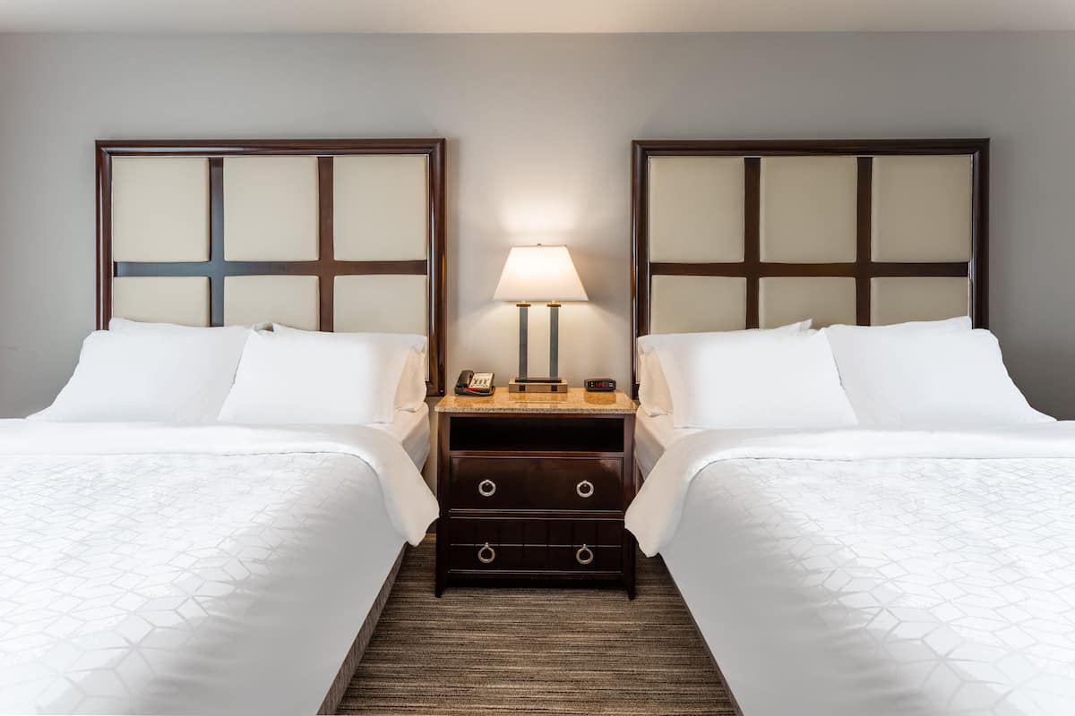 Een hotelkamer met twee bedden, een nachtkastje met een lamp en een klein dressoir.