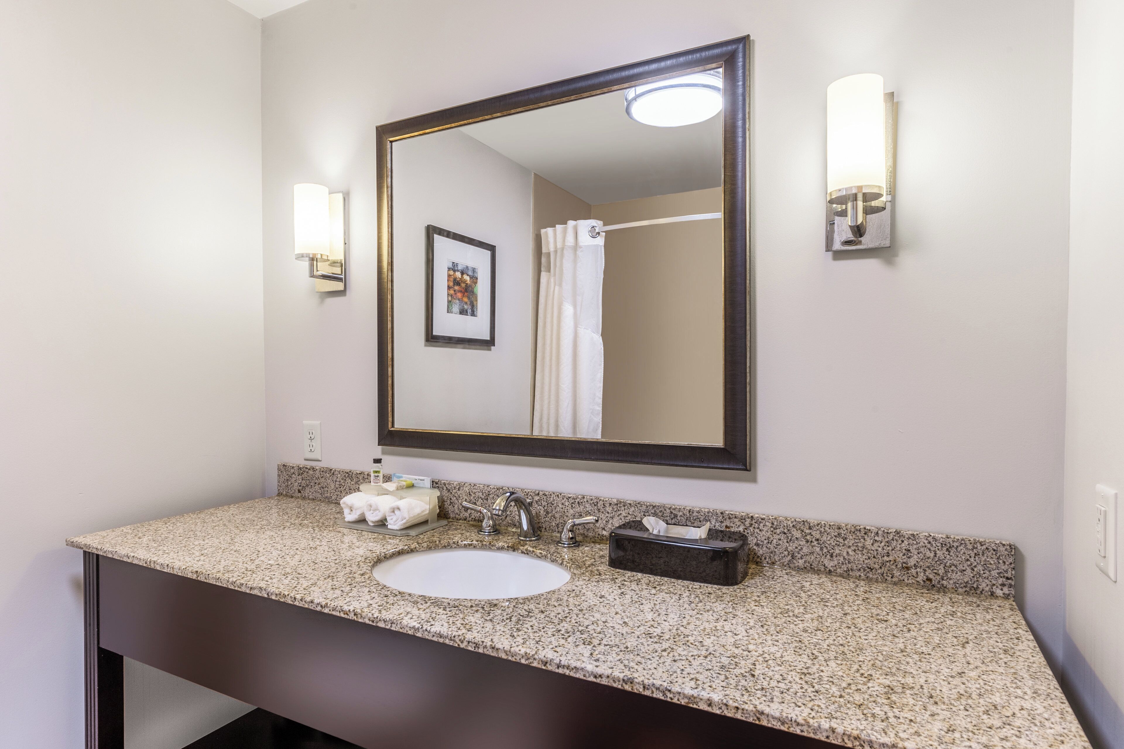 A bathroom with a granite countertop, a white sink, a mirror, and a framed picture on the wall.