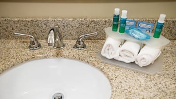 Un lavamanos con tres grifos, un lavabo blanco y un dispensador de jabón con artículos de aseo.