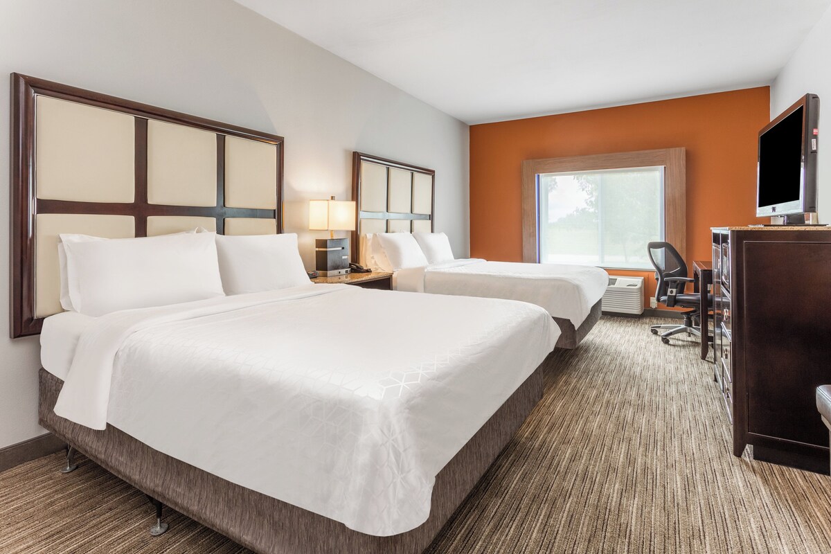 A hotel room with two beds, a desk with a chair, a television, and a large window.
