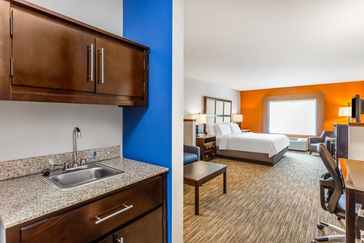 Een hotelkamer met kitchenette, een bed, een bureau en een groot raam.