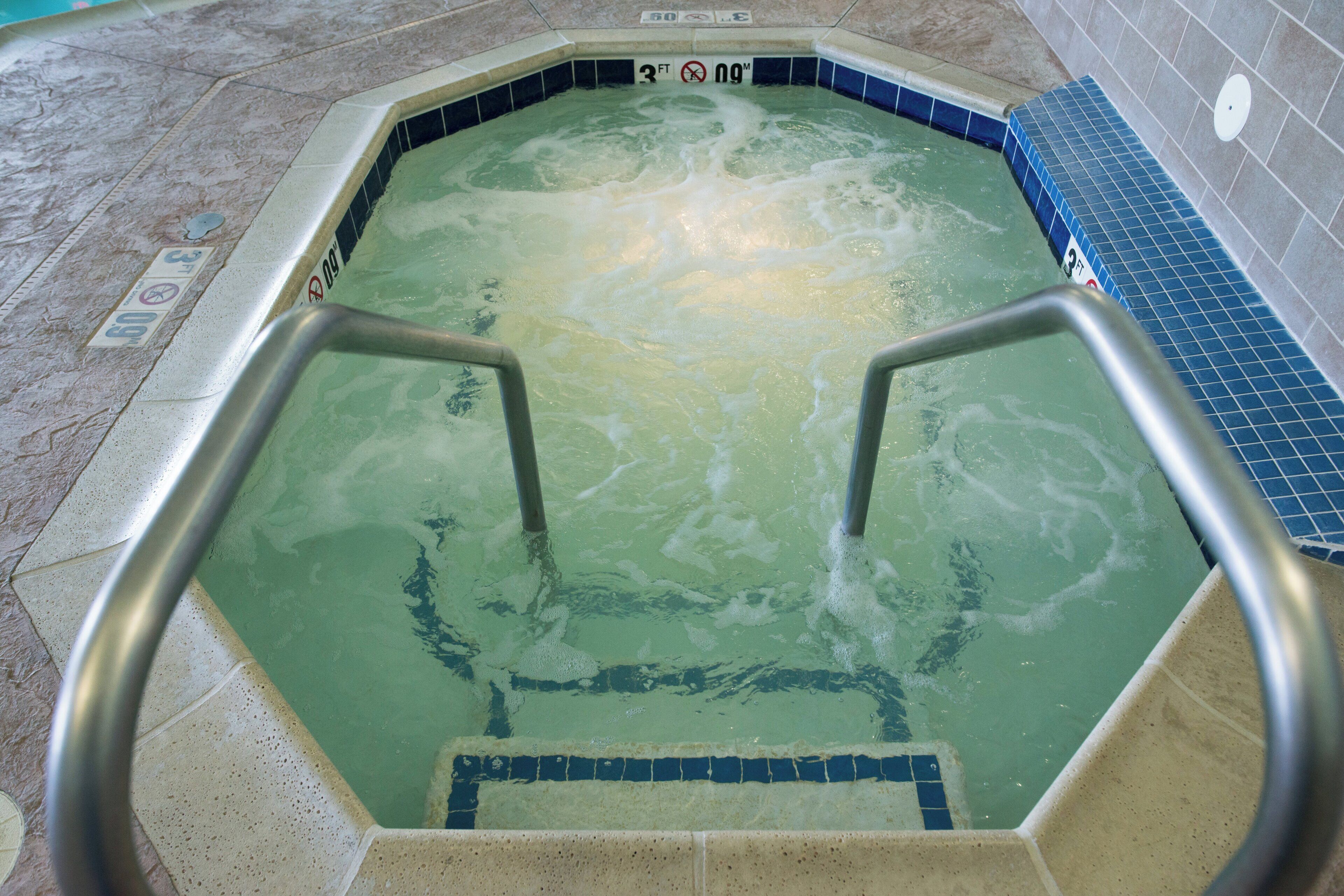 A hot tub with a tiled interior, metal steps, and a blue tiled wall.