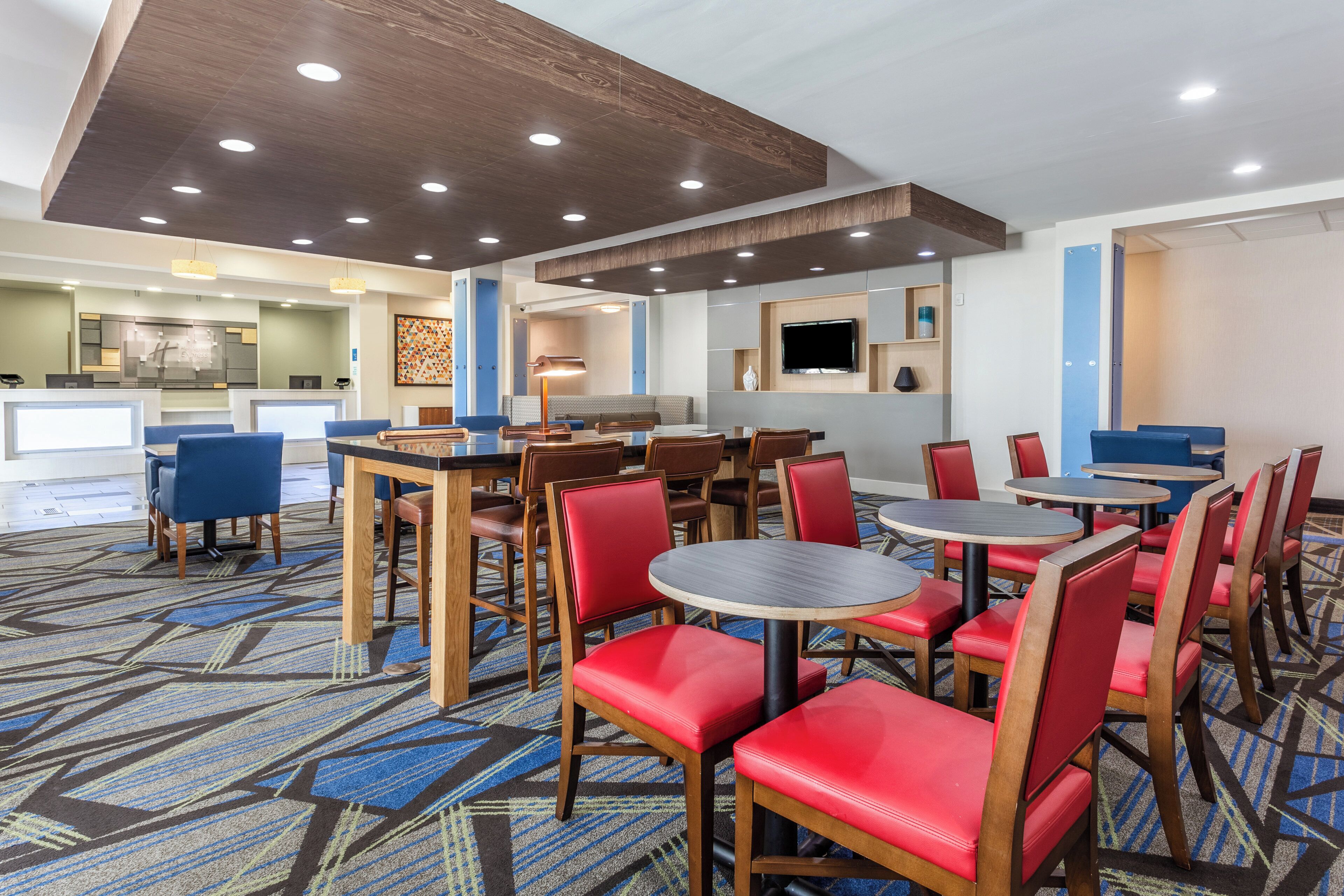 A hotel dining area with multiple tables and chairs, a reception desk, and a television screen on the wall.