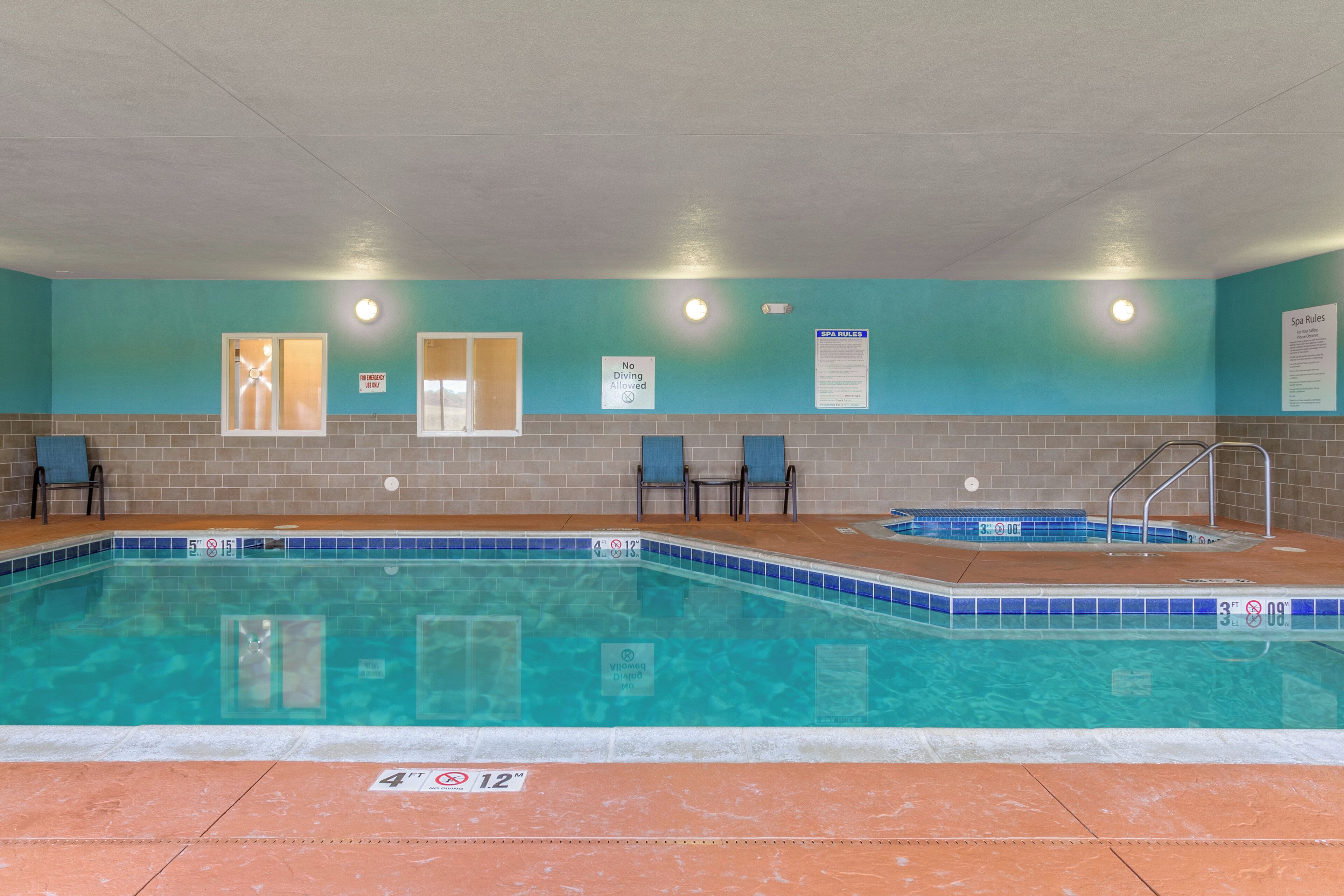 Una piscina con borde de azulejos, un jacuzzi y una pared con carteles de normas de seguridad y spa.
