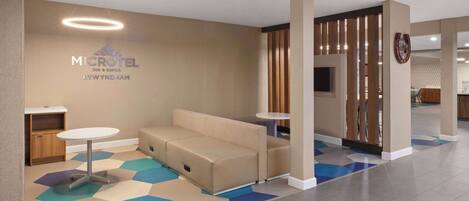 A modern hotel lobby with a sofa, two small tables, and a decorative wall with the hotel name.