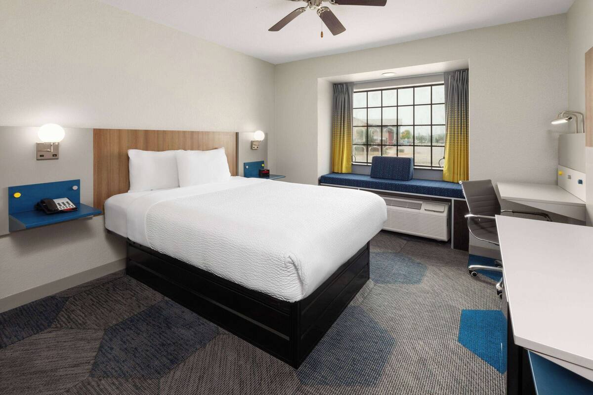 A hotel room with a bed, desk, chair, and a window with curtains.
