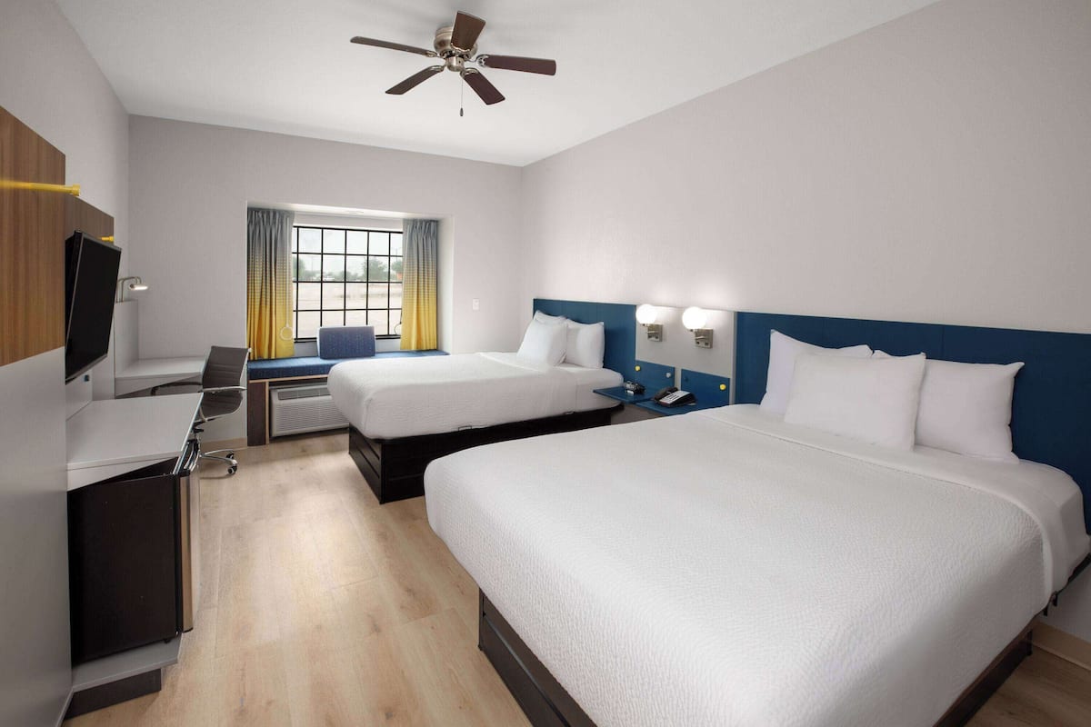 A hotel room with two beds, a desk, a TV, and a ceiling fan.