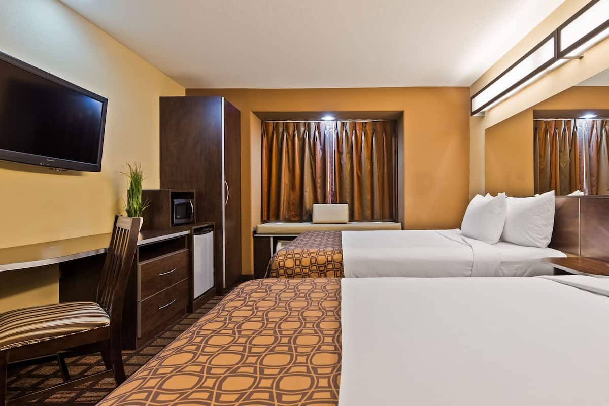 A hotel room with a bed, a desk, a chair, a TV, and curtains.
