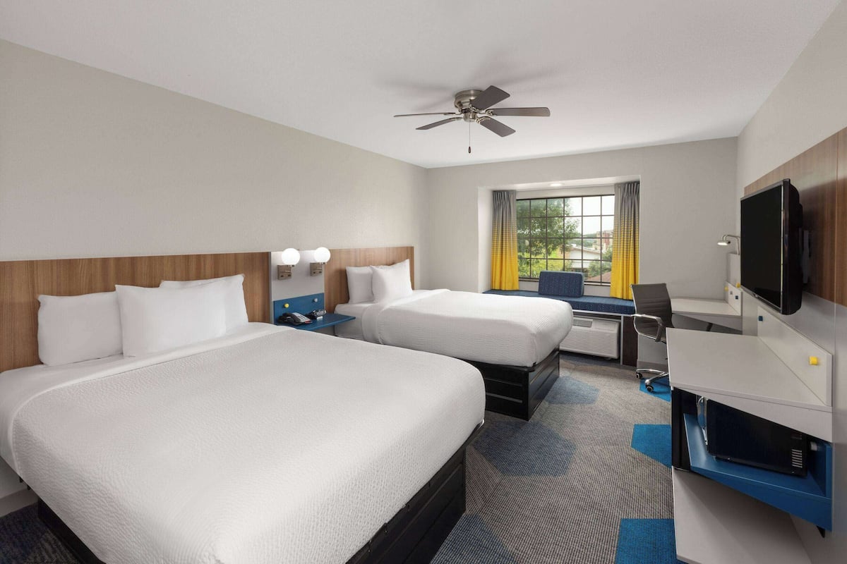 A hotel room with two beds, a desk, a television, and a ceiling fan.