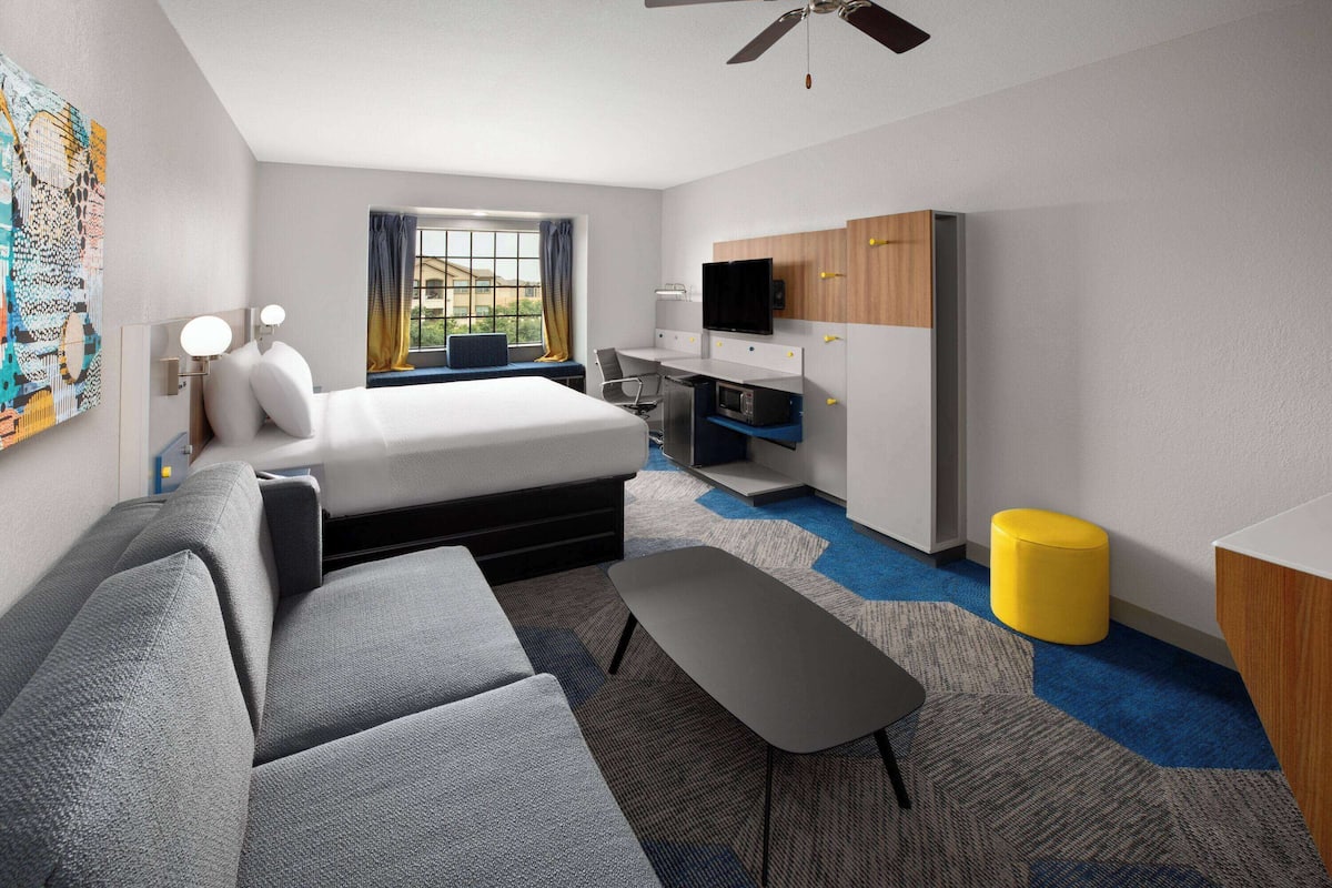 A modern hotel room with a bed, sofa, desk, and TV.