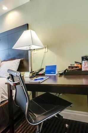 Ein Hotelzimmer mit einem Bett, einem Schreibtisch mit einem Laptop, einem Stuhl, einer Lampe und einem Telefon.