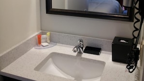 A hotel bathroom with a large mirror, a sink, a hairdryer, and toiletries on the counter.