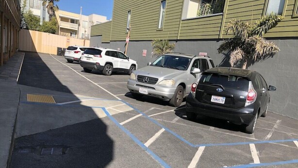A parking lot with several cars parked, including a white SUV, a silver sedan, and a black compact car.