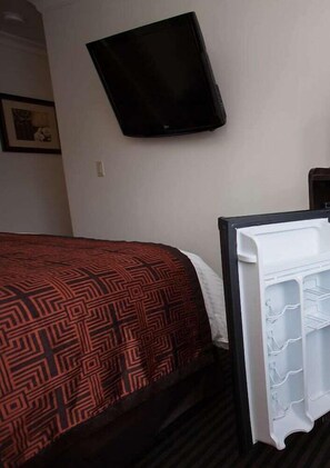 A hotel room with a bed, a TV mounted on the wall, and a white bedside table with a tray. - Seaside Inn (San Francisco)