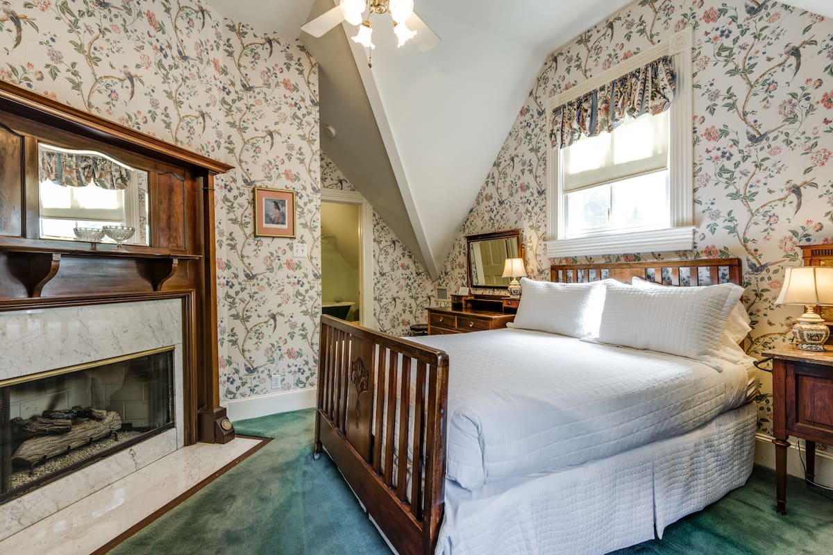 Quarto com uma cama grande, penteadeira de madeira, lareira e papel de parede floral.