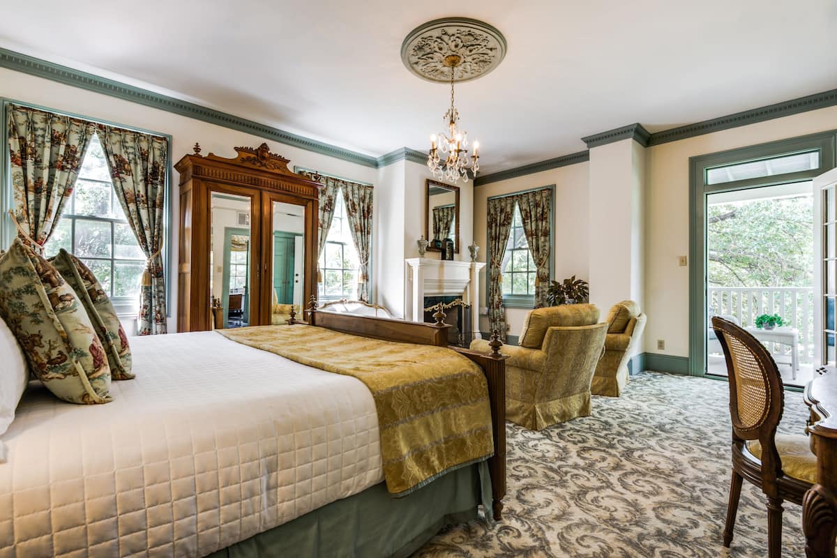 Um quarto espaçoso com uma cama grande, uma cômoda de madeira, um espelho e um candelabro.