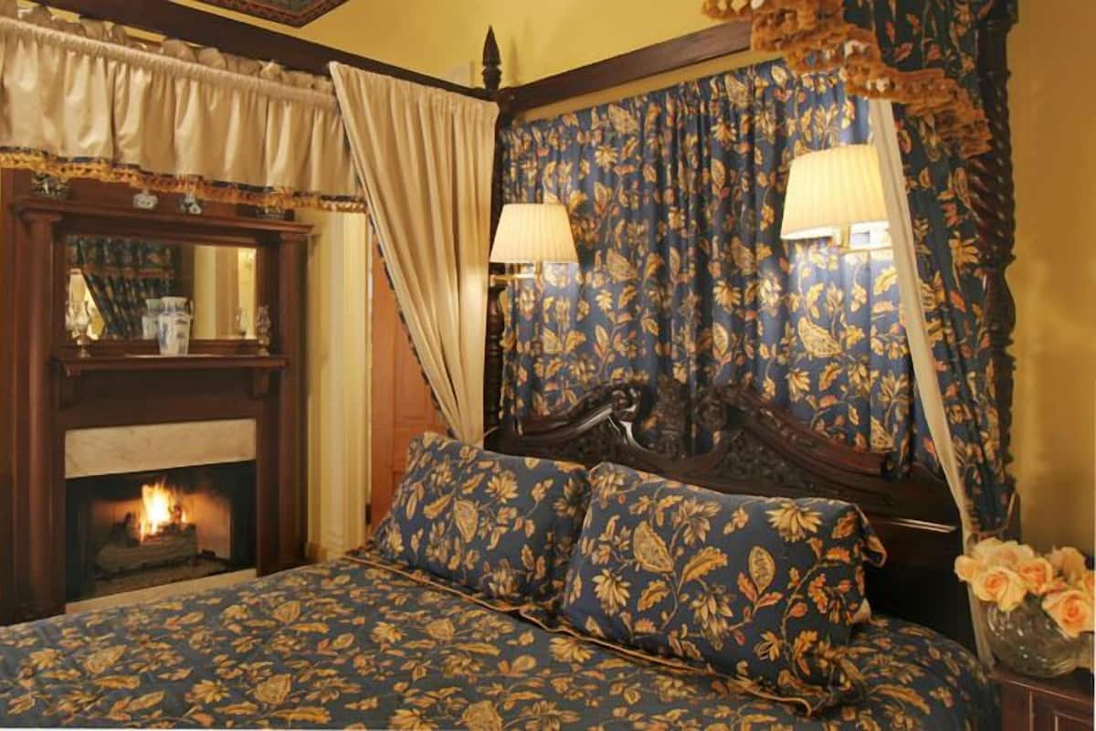 Quarto com cama de dossel, lareira e cortinas florais.