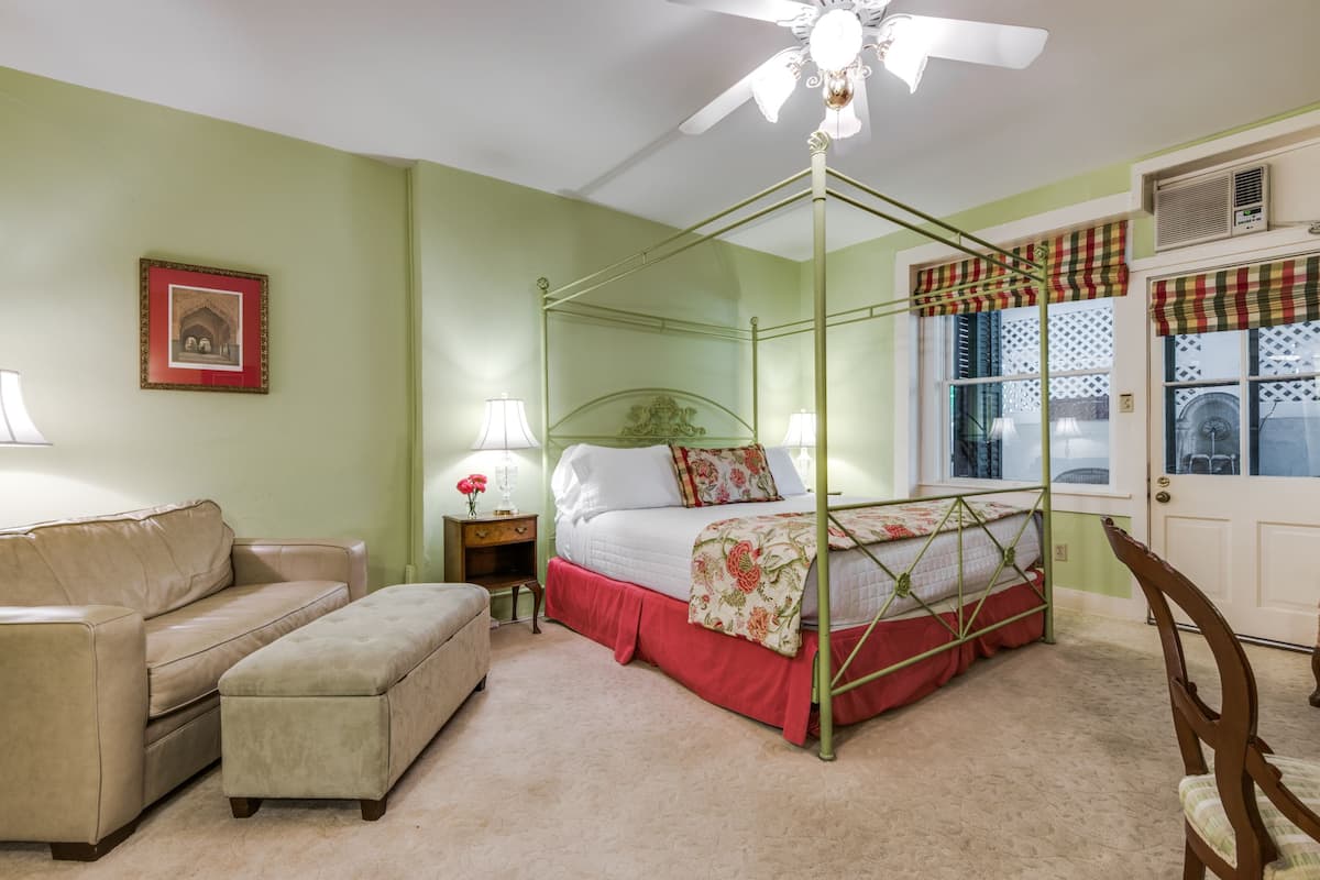 Um quarto com uma cama de dossel, um sofá, um banquinho, uma mesa de cabeceira com uma luminária e um quadro na parede.