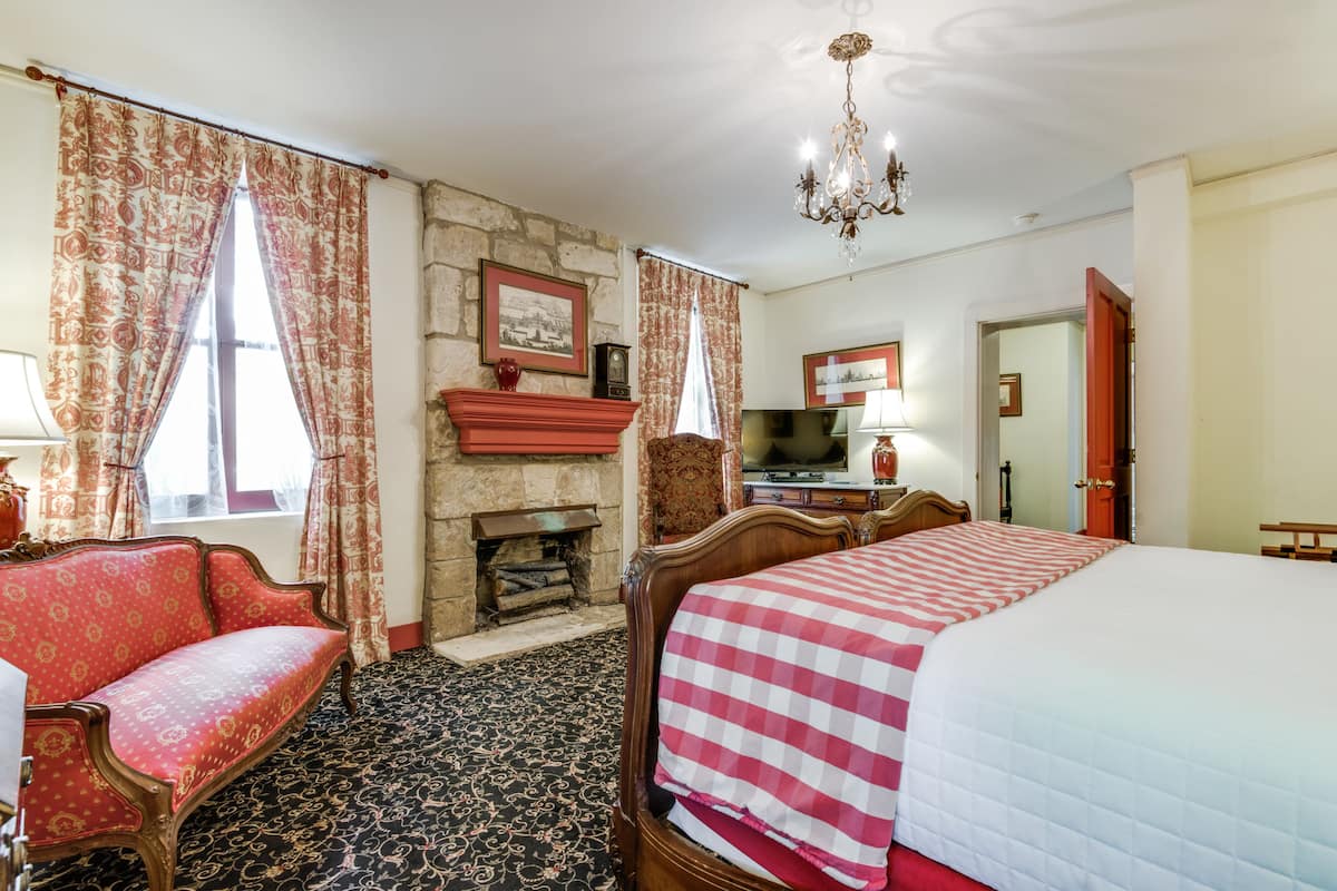 Quarto de hotel com uma cama grande, um sofá vermelho, lareira, televisão e um candelabro.