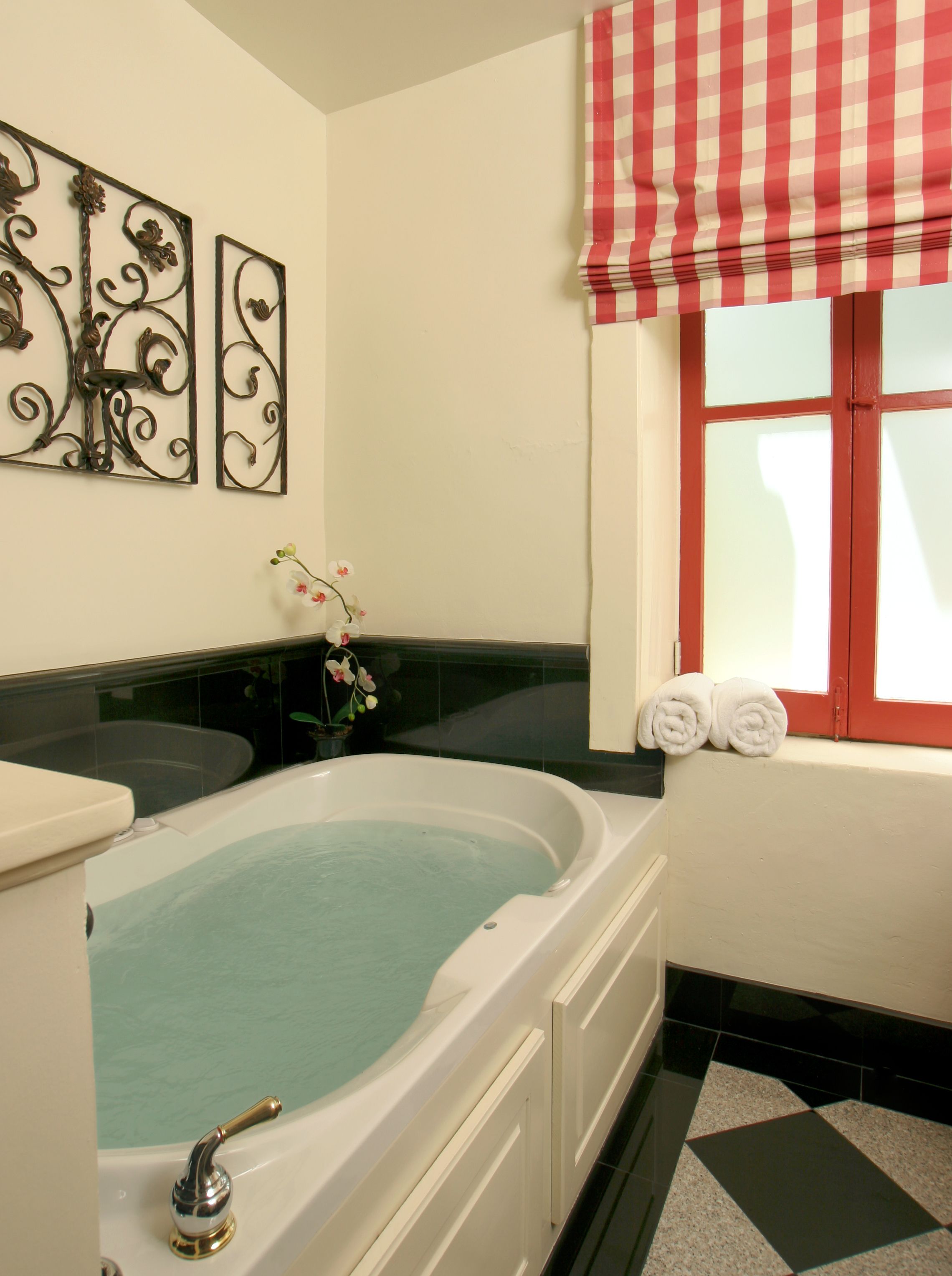 Ein Badezimmer mit einer Badewanne, einem Fenster mit rot-weiß kariertem Vorhang und dekorativen Wandbildern.