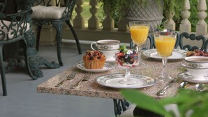 An outdoor dining area with a table set for breakfast, including a muffin, fruit salad, and orange juice. - Noble Inns (San Antonio)