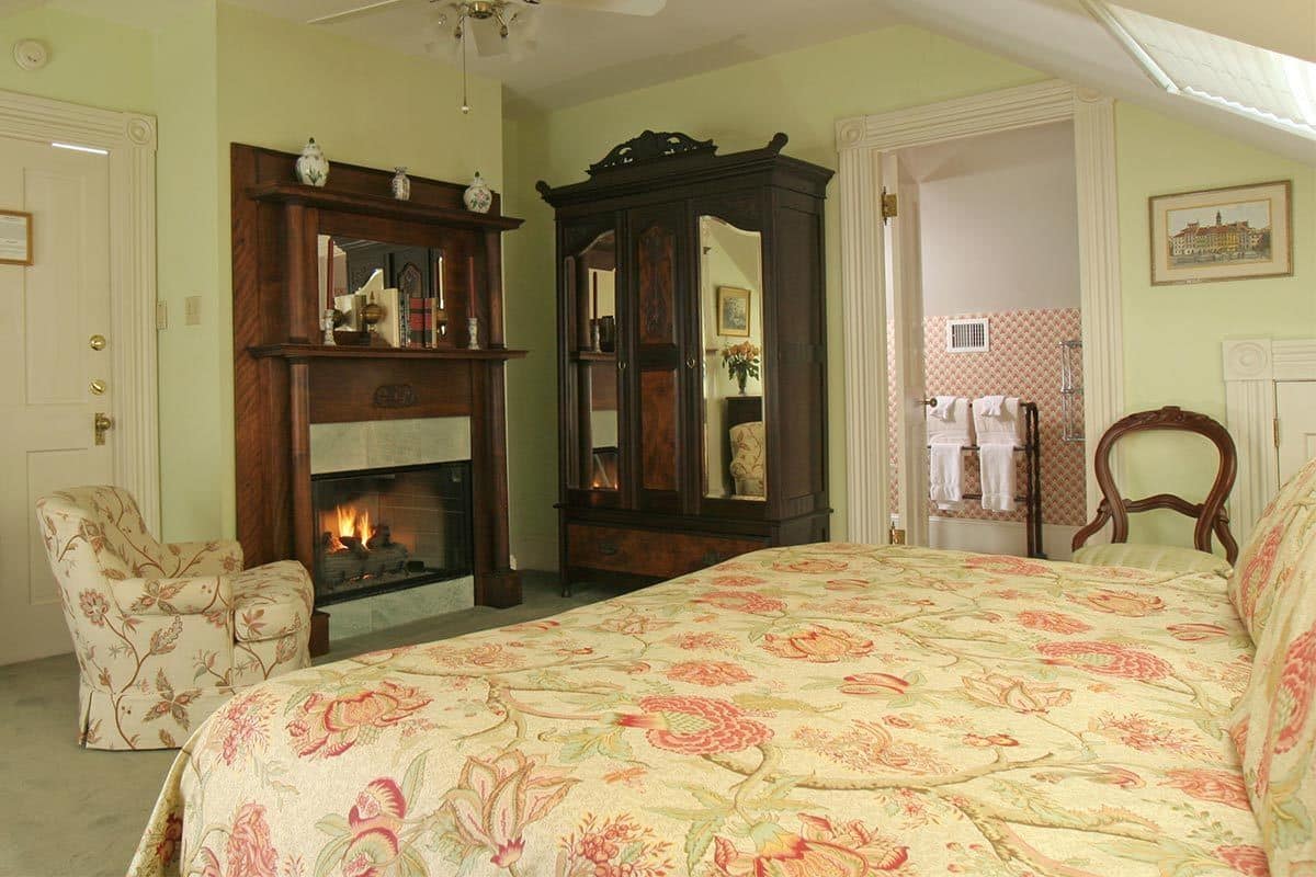 Quarto com uma cama grande, lareira, armário de madeira e uma cadeira.