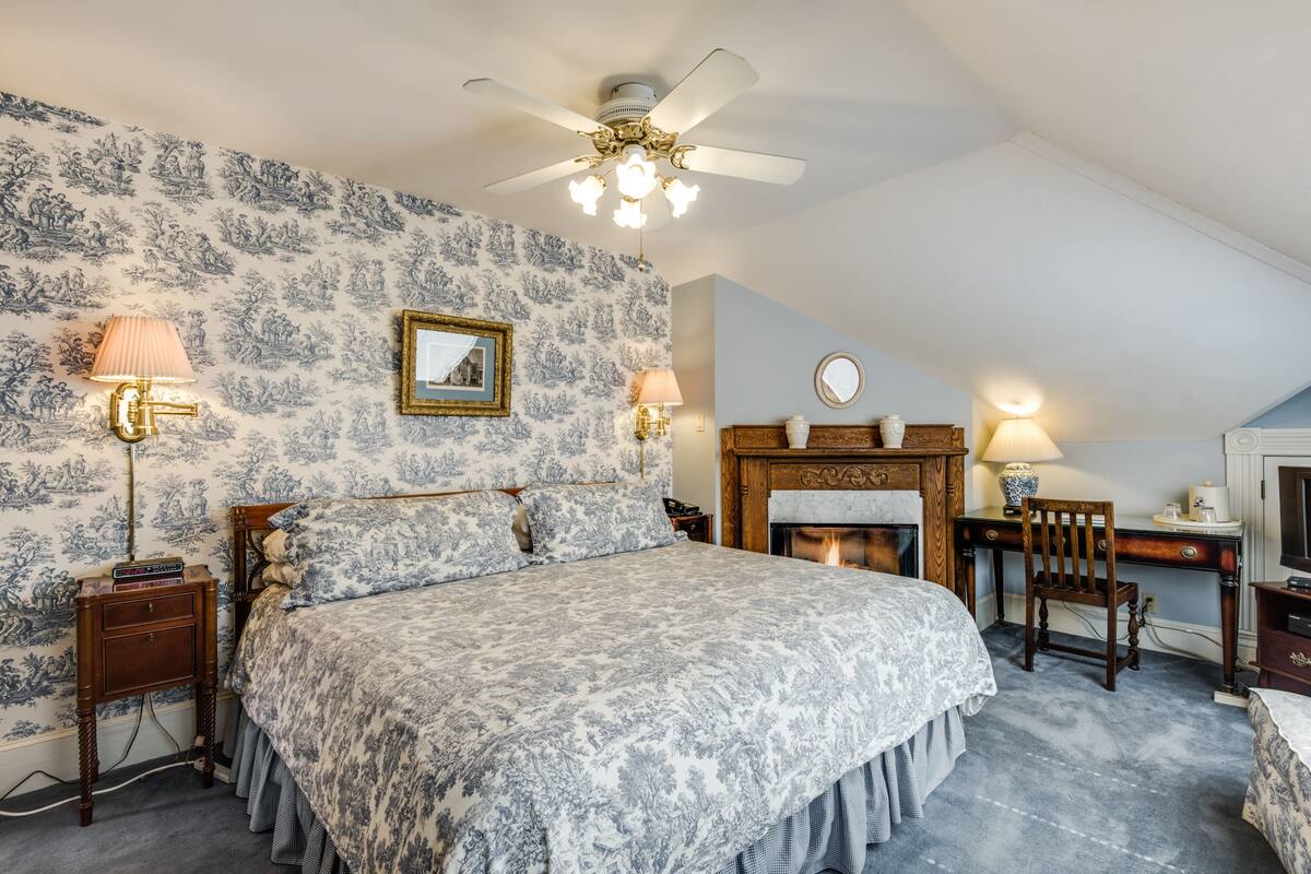Quarto com cama grande, escrivaninha de madeira, lareira e ventilador de teto.