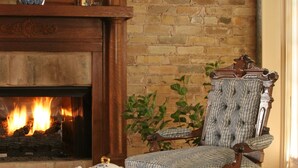 A cozy living room with a fireplace, a comfortable armchair, a wooden coffee table with a tray of tea and snacks, and a patterned rug. - Noble Inns (San Antonio)