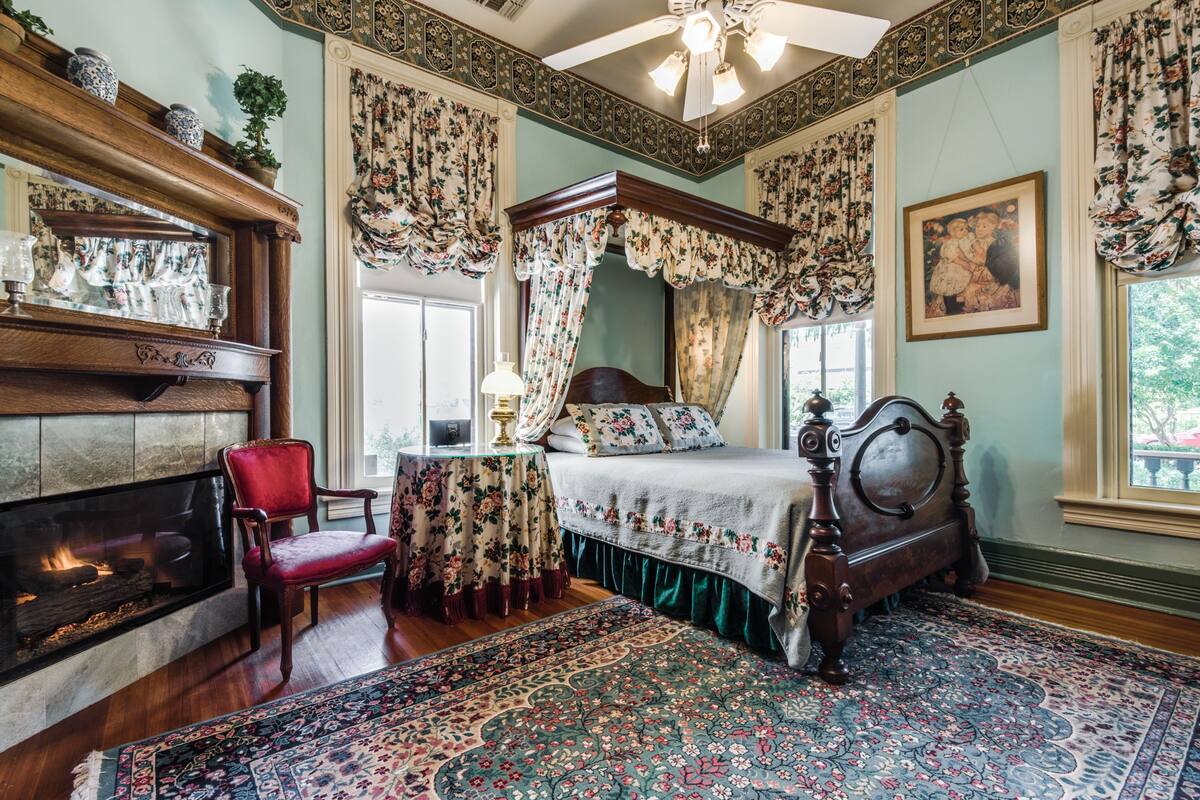 Um quarto tradicional com cama de dossel, lareira e cortinas florais.