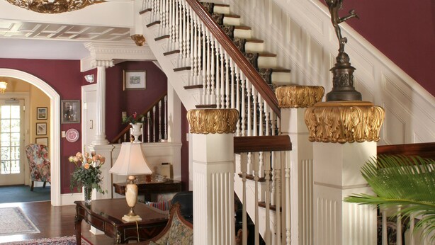 A grand staircase with ornate balusters and a chandelier, leading to an upper floor. - Noble Inns (San Antonio)