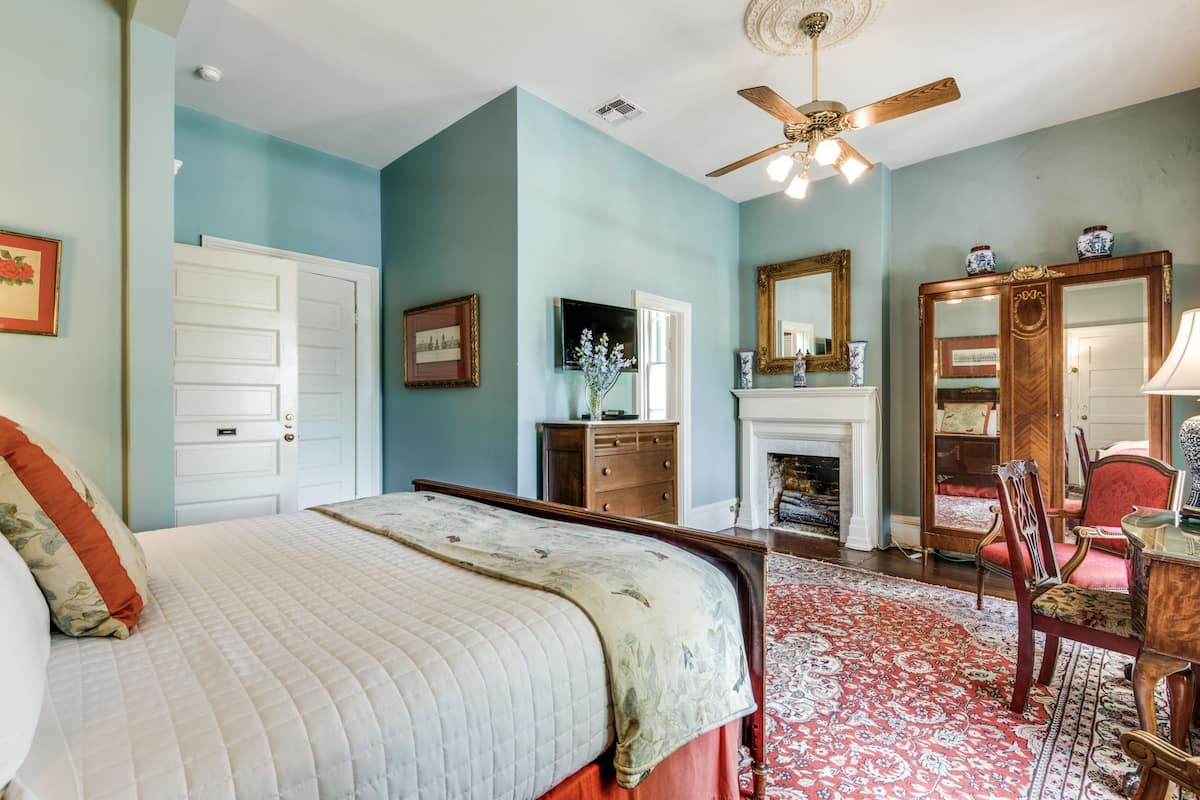 Quarto com cama, cômoda, espelho, lareira e ventilador de teto.