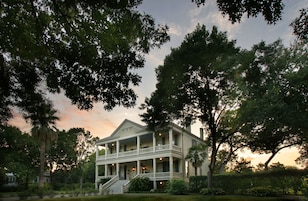 A two-story colonial-style building with a central balcony and a staircase leading to the entrance.
