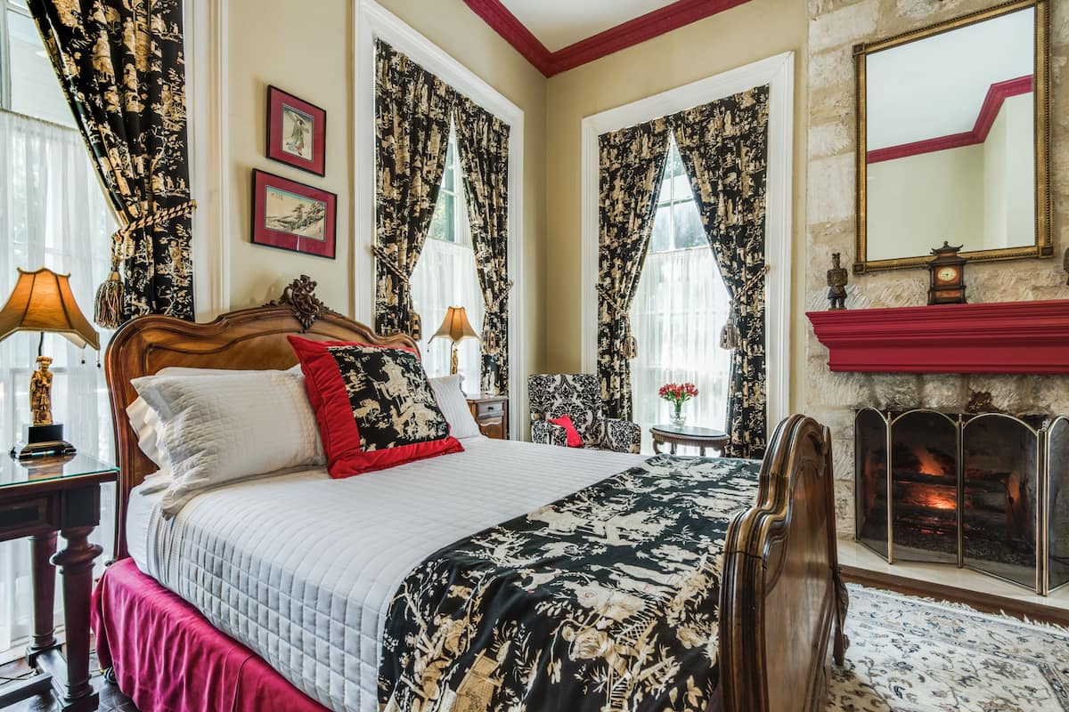 Quarto de hotel clássico com uma cama grande, lareira e cortinas ornamentadas.