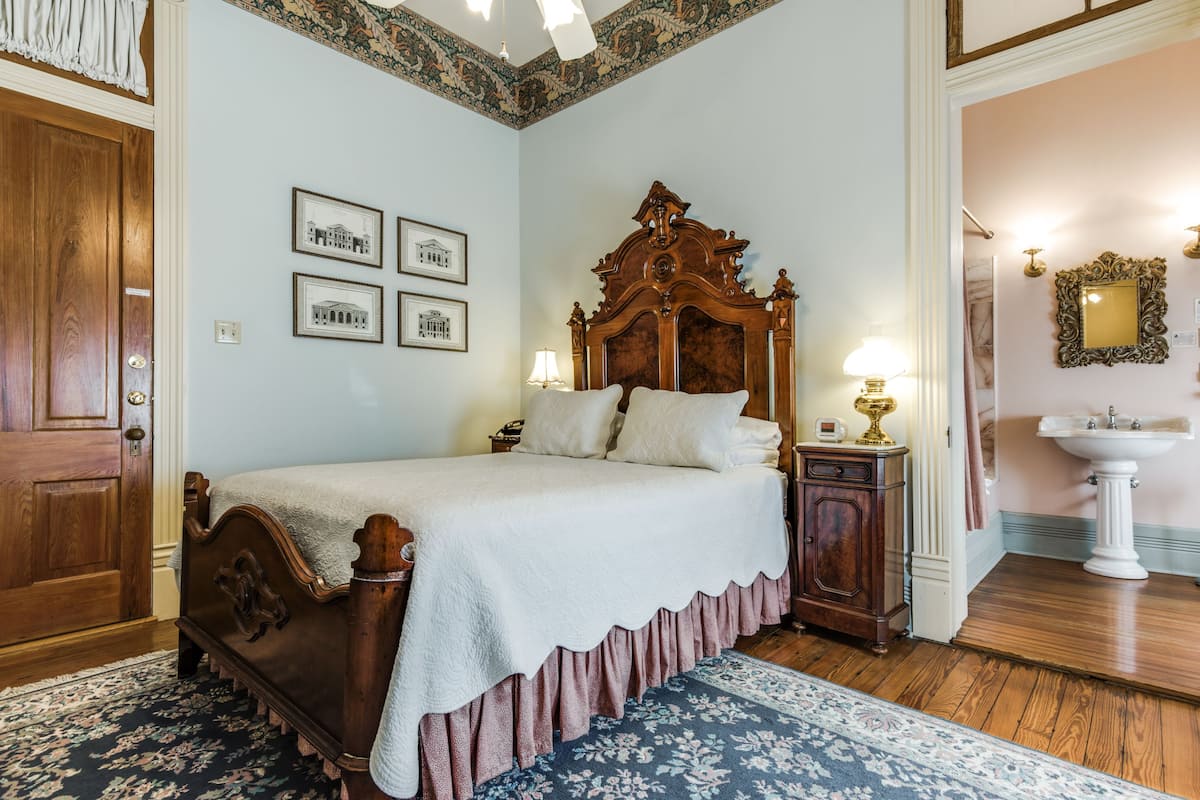 Quarto com cama de madeira, mesa de cabeceira, penteadeira, espelho e quadros nas paredes.
