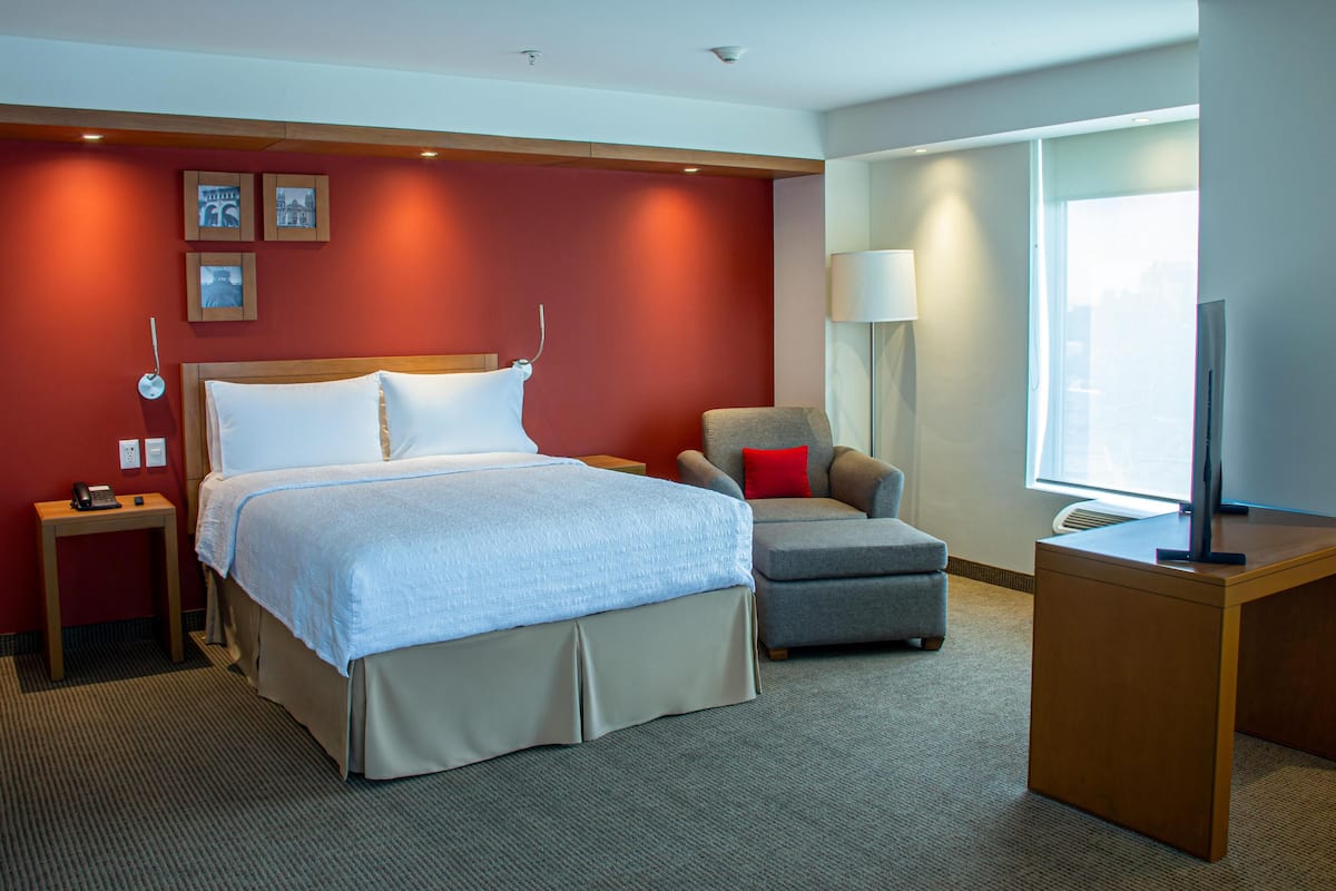 Habitación de hotel con cama, escritorio, silla, lámpara y televisor.