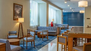 Un vestíbulo de hotel con zonas de estar, un mostrador de recepción y una amplia pared azul con un mensaje de bienvenida.