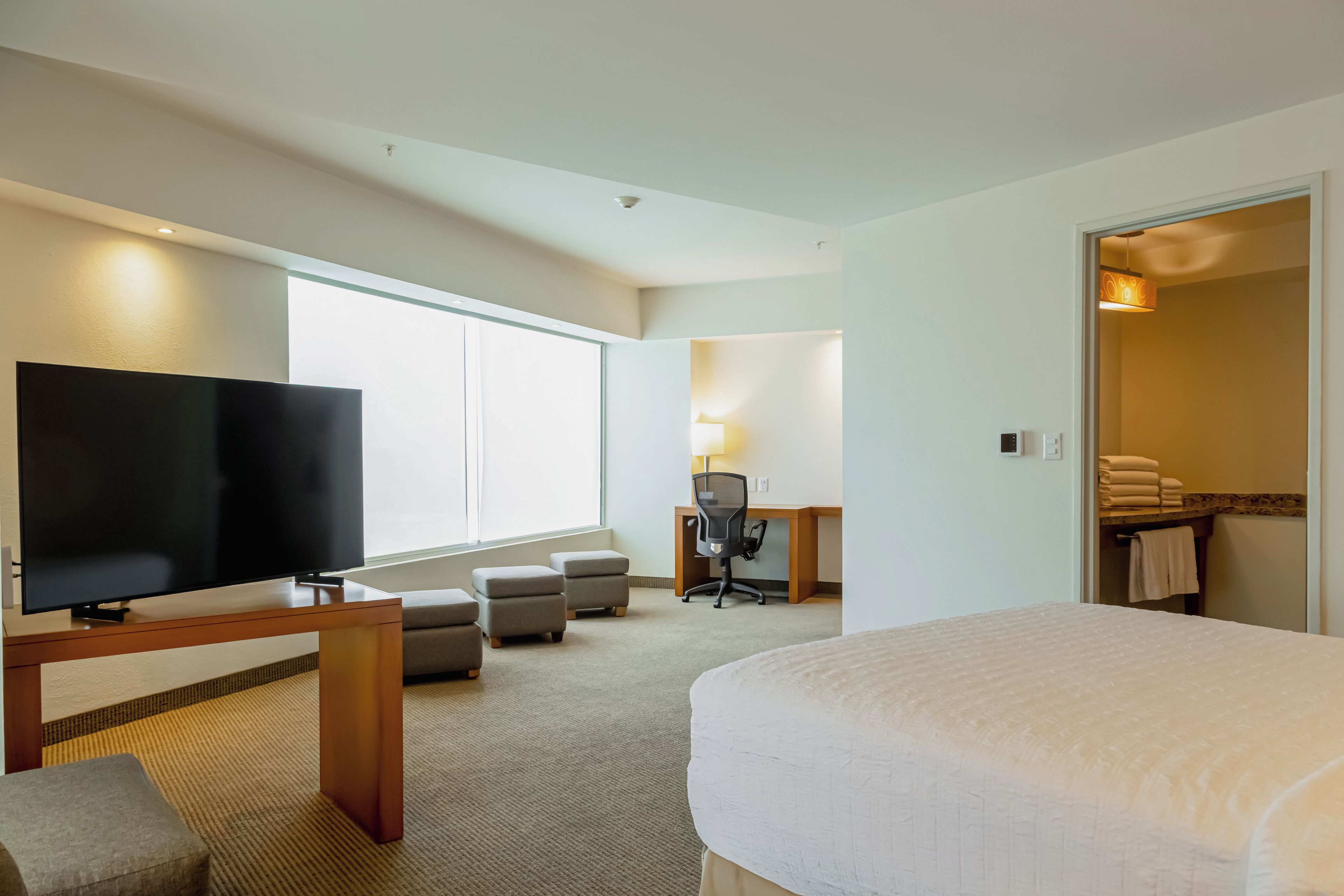 A hotel room with a bed, a TV, a desk with a chair, and a bathroom visible through an open door.
