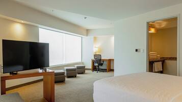 A hotel room with a bed, a TV, a desk with a chair, and a bathroom visible through an open door.